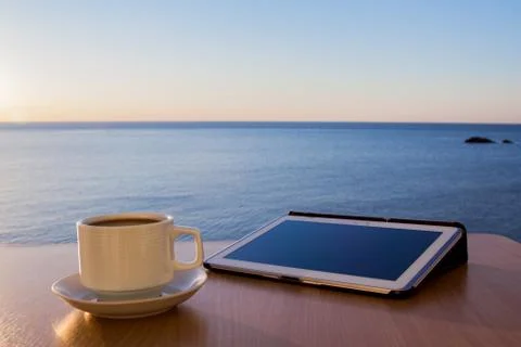 White tablet ipad on table desk with coffee cup, with sea landscape Stock Photos