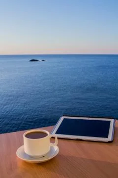 White tablet ipad on table desk with coffee cup, with smooth sea landscape Stock Photos