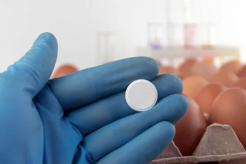 White tablet lying in the hand of an expert on a background of eggs in a tray Stock Photos