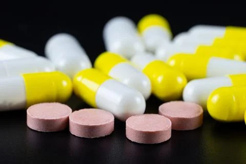White tablet with two pills in background. Black background with reflection Stock Photos