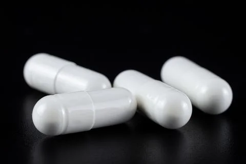 White tablet with two pills in background. Black background with reflection. Stock Photos