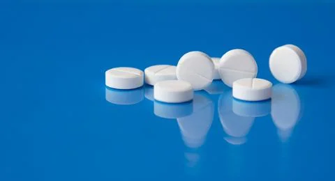 White tablets lie on a blue reflective surface Stock Photos
