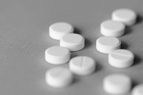 White tablets scattered on a gray surface close up. Black and white Stock Photos
