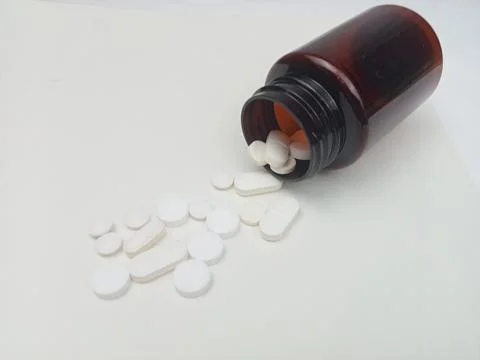 White tablets spilling from brown bottle on white background Stock Photos