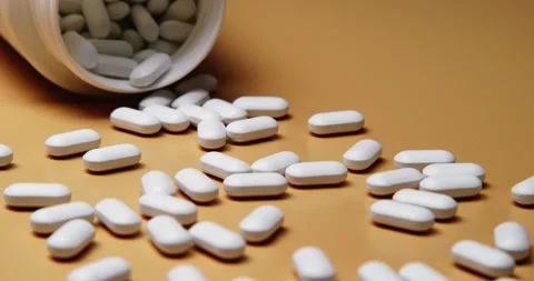 White tablets spilling out of open bottle on to surface Stock Footage 303056704