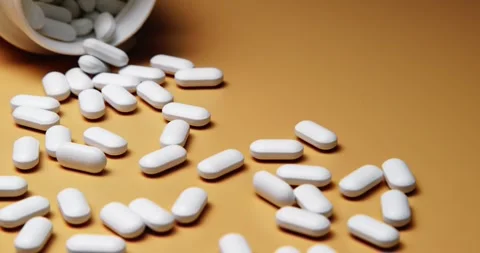 White tablets spilling out of open bottle on to surface 動画素材 303056779