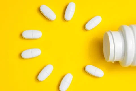 White tablets on a yellow background fall out of a white jar. Stock Photos