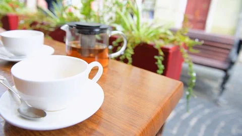 White tea cup on table at sidewalk cafe with people walking in blurry background Stock Footage 112757170