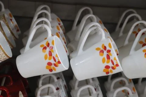 White tea cups with red and yellow leaf pattern hang neatly on white holders Stock Photos