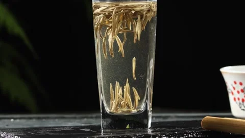 White tea leaves floating in a clear glass of water moody dark background Stock Footage 341668703