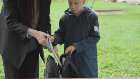 White teacher guides boy packing backpack park setting hands inserting folder Stock Footage 333094301