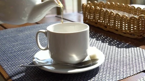 White teapot pouring tea into cup in slow motion. Cafe interior. Sunlight Stock Footage 80789229