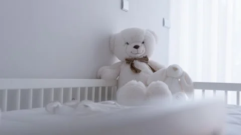 White Teddy Bear with Bow and Plush Bunny in Bright Baby Crib Stock Footage 343707798