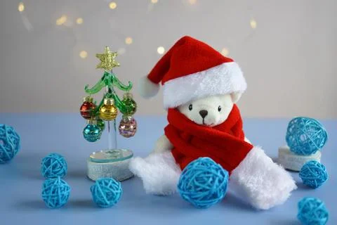 A white teddy bear in a red hat and Santa Claus scarf sits near a glass ele.. Foto stock