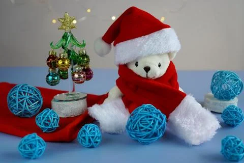 A white teddy bear in a red hat and Santa Claus scarf sits near a glass ele.. 스톡 사진