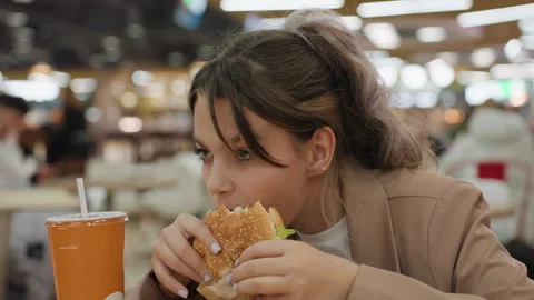 White teen student devouring burger at busy food court, eager bites, orange Stock Footage 321599611