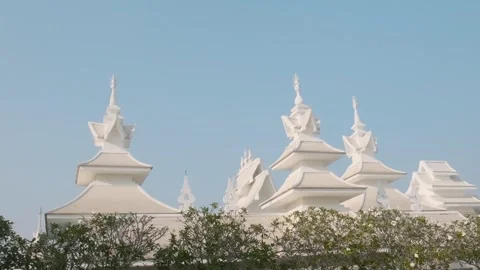 White temple rooftops with ornate spires rising above green trees under clear Stock Footage 315855004