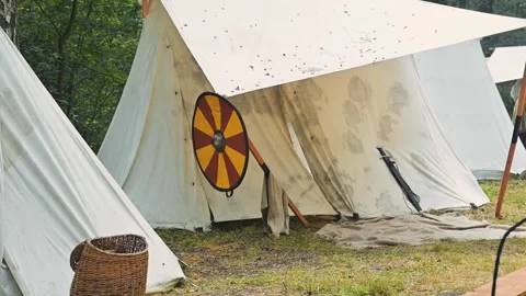 White tents in a green field, creating a natural atmosphere. A shield rests Stock Footage 345036995
