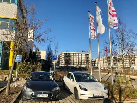 A white Tesla Model 3 and a black Tesla Model S car are charging at a public Stock Photos