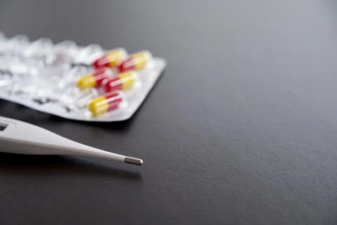 White thermometer on a dark table with a carton of colored pills. Fever conce Stock Photos