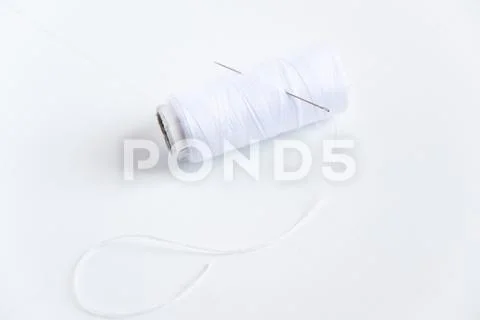 White thread and sewing needle on white background with space for text. Minimal Stock Photos