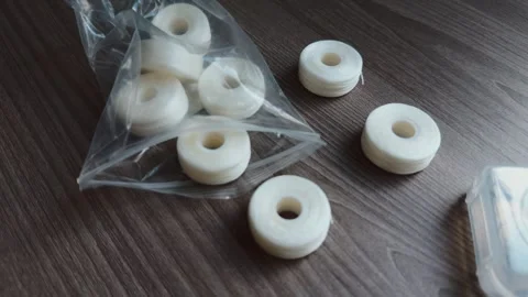 White thread bobbins and spools sit on dark tabletop, partly gathered in clear Stock-Footage 347218945