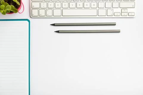 White, tidy workspace setup with a computer keyboard, a plant, pens, and a noteb Foto stock