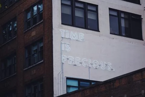 A white time is precious neon on a building facade Stock Photos