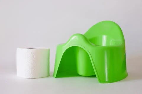 White toilet paper and stack of diapers beside green potty on white background Stock Photos