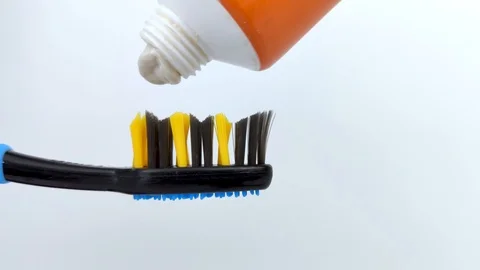 White toothpaste is gently squeezed out of the tube onto a dark blue brush. Macr Stock Footage 125084542