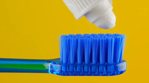 White toothpaste is placed on a blue toothbrush on a yellow background close-up. Stock Footage 147648887