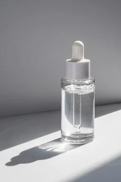 A white transparent bottle with serum in the rays of the sun. Stock Photos