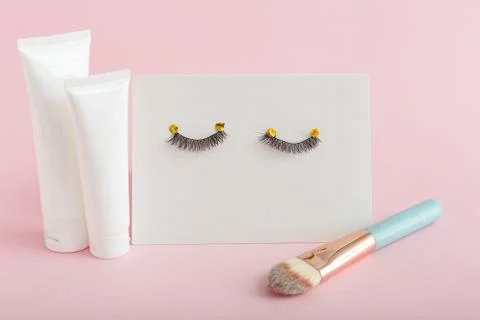 White tubes with mock up for design. False eyelashes, makeup brush on pink ba Stock Photos