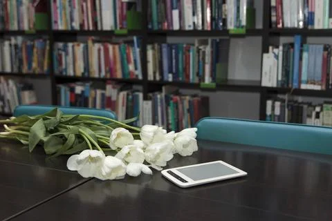 White tulips and e-reader on library table with bookshelves in background Stock-Fotos