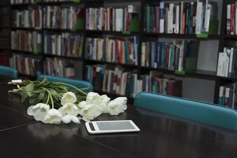 White tulips and modern e-reader on library table with bookshelves in backg.. Stock Photos