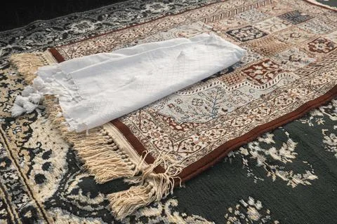 A white turban and a brown patterned prayer mat on a green carpet. The pray.. Stock Photos