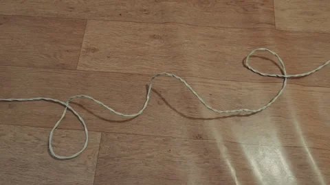White twisted string slithers like a snake across a light brown wooden floor Stock Footage 346539867
