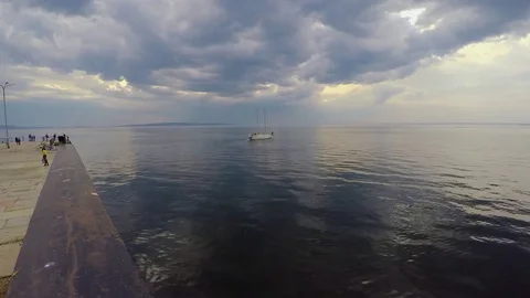 White two-masted yacht leaves the concrete pier under a cloudy sky and calm Stock Footage 75627770