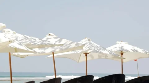 White umbrellas blowing in the wind with the turquoise green ocean in the bac Stock Footage