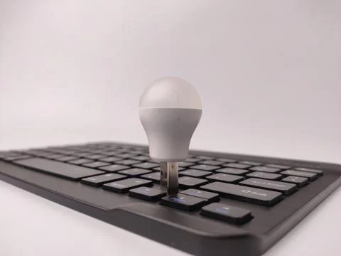 A white USB-powered light bulb stands upright, inserted between the keys of.. Stock Photos