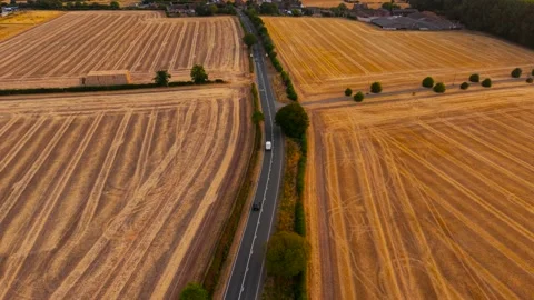 White van and black sedan driving along rural road between harvested Stock Footage 345126153
