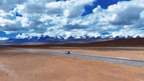White Van Driving on Remote Desert Road with Snow-Capped Mountains Tibet China 動画素材 346737992