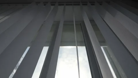 White vertical blinds gradually opening, filtering sunlight through window Stock Footage 331923940