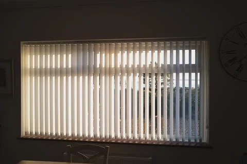 White vertical blinds on a window with bright sunlight behind them. Stock Photos