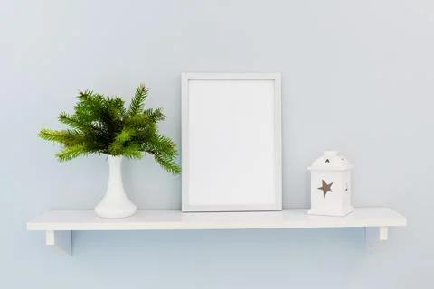 A white vertical frame stands on a shelf with fir branches and a candlestick Stock Photos