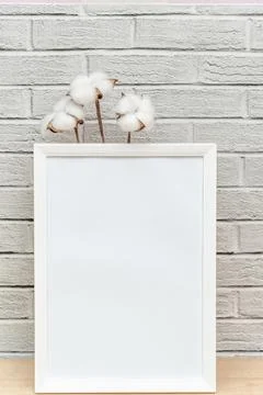 White vertical frame on a wooden table and cotton flowers on brik wall Stock Photos