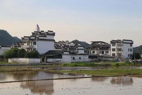 White village buildings reflected in flooded fields beneath green hills and.. Stock Photos