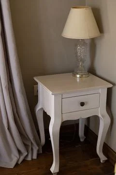 White vintage bedside table with drawer and crystal lamp in bedroom corner Stock Photos