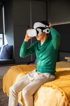 White virtual reality headset is being adjusted on bed in modern bedroom with Stock Photos