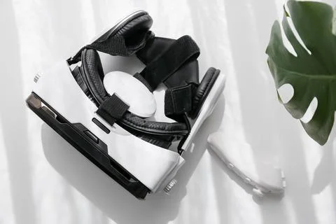 White virtual reality headset with controller and monstera leaf on clean back Stock Photos
